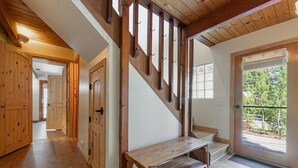 Una escalera de madera con un banco al pie, que lleva a una puerta con vistas a la vegetación.