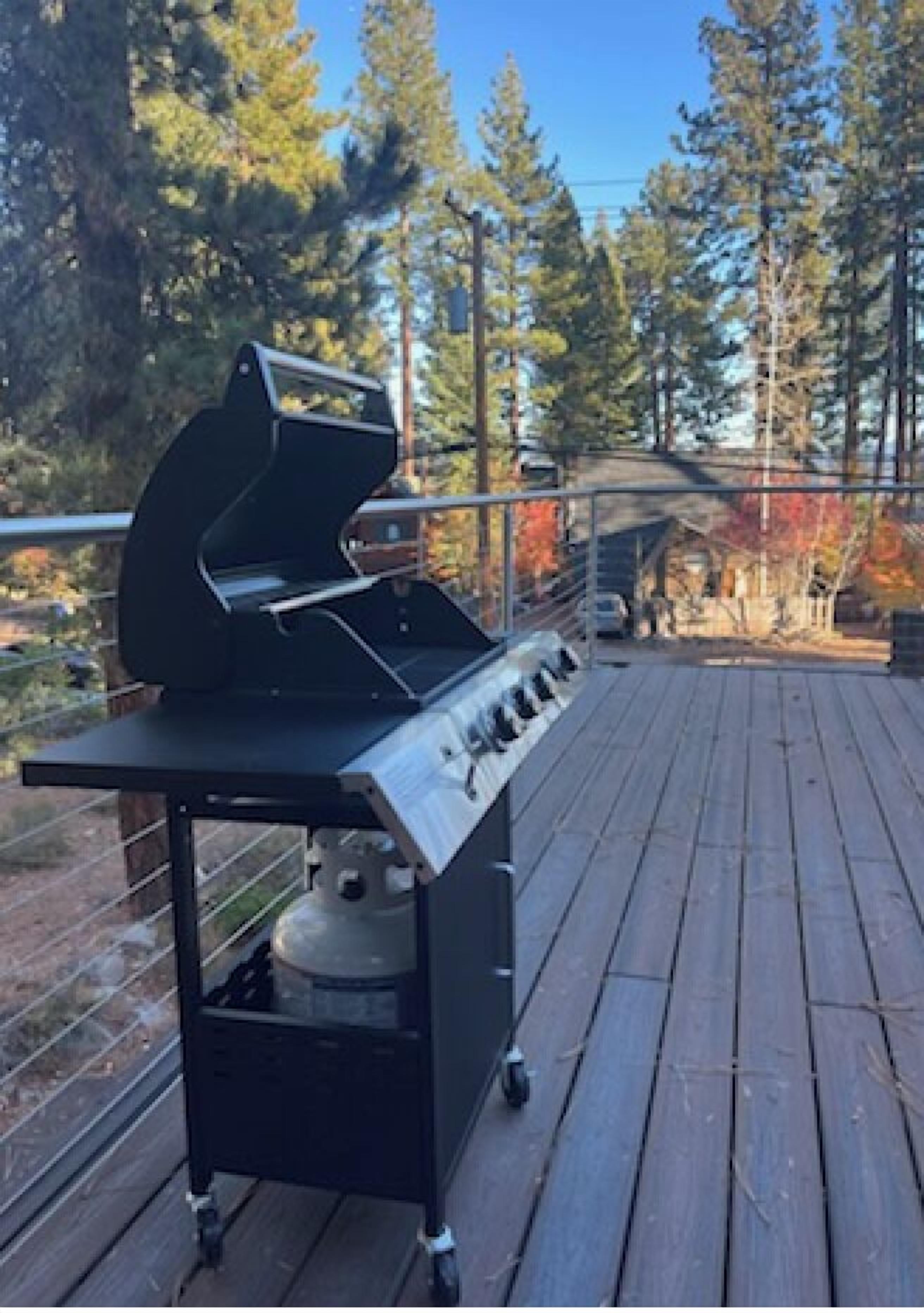 A barbecue grill on a wooden deck with a view of trees and a house in the background.