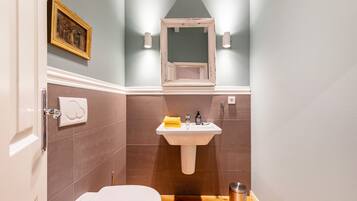 Een badkamer met een wit toilet, een wastafel met een gele handdoek, een lijstspiegel en een afbeelding aan de muur.