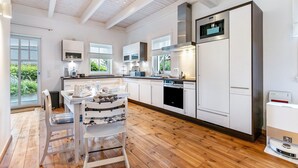 Een moderne keuken met witte kasten, een eethoek met tafel en stoelen, en uitzicht door het raam.