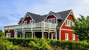 Een rood gebouw met een balkon, meerdere ramen en een tuin ervoor.