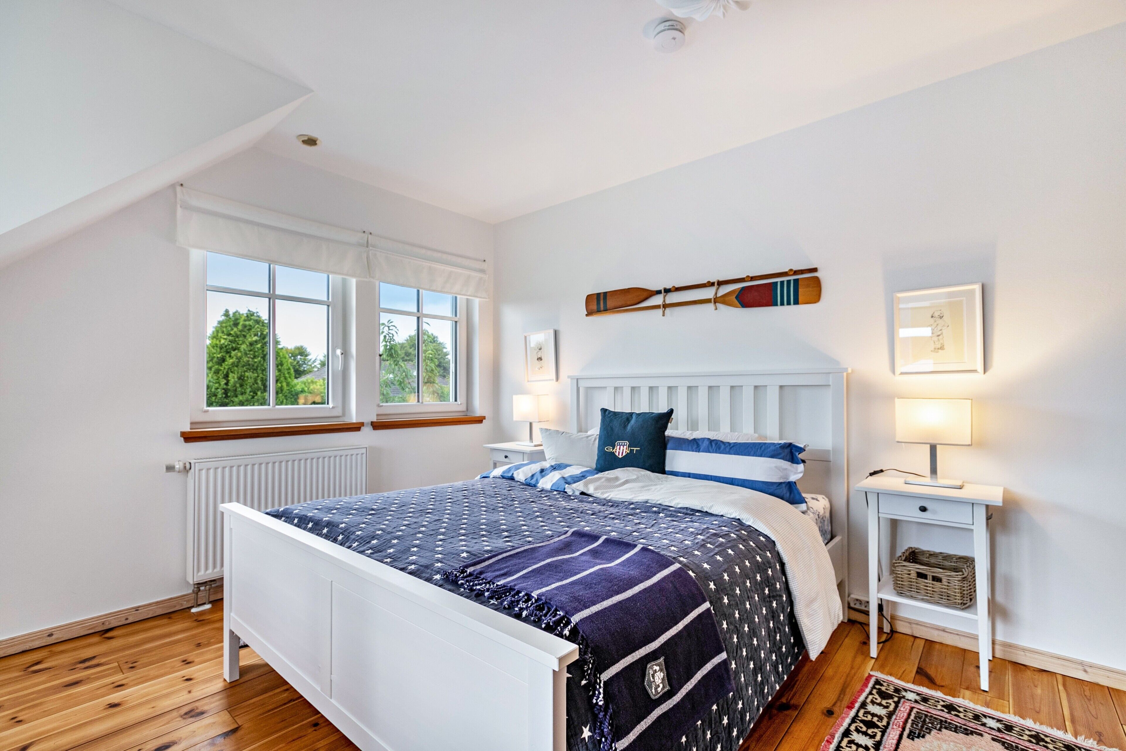 A bedroom with a bed, a window, a nightstand, and a wall-mounted shelf.