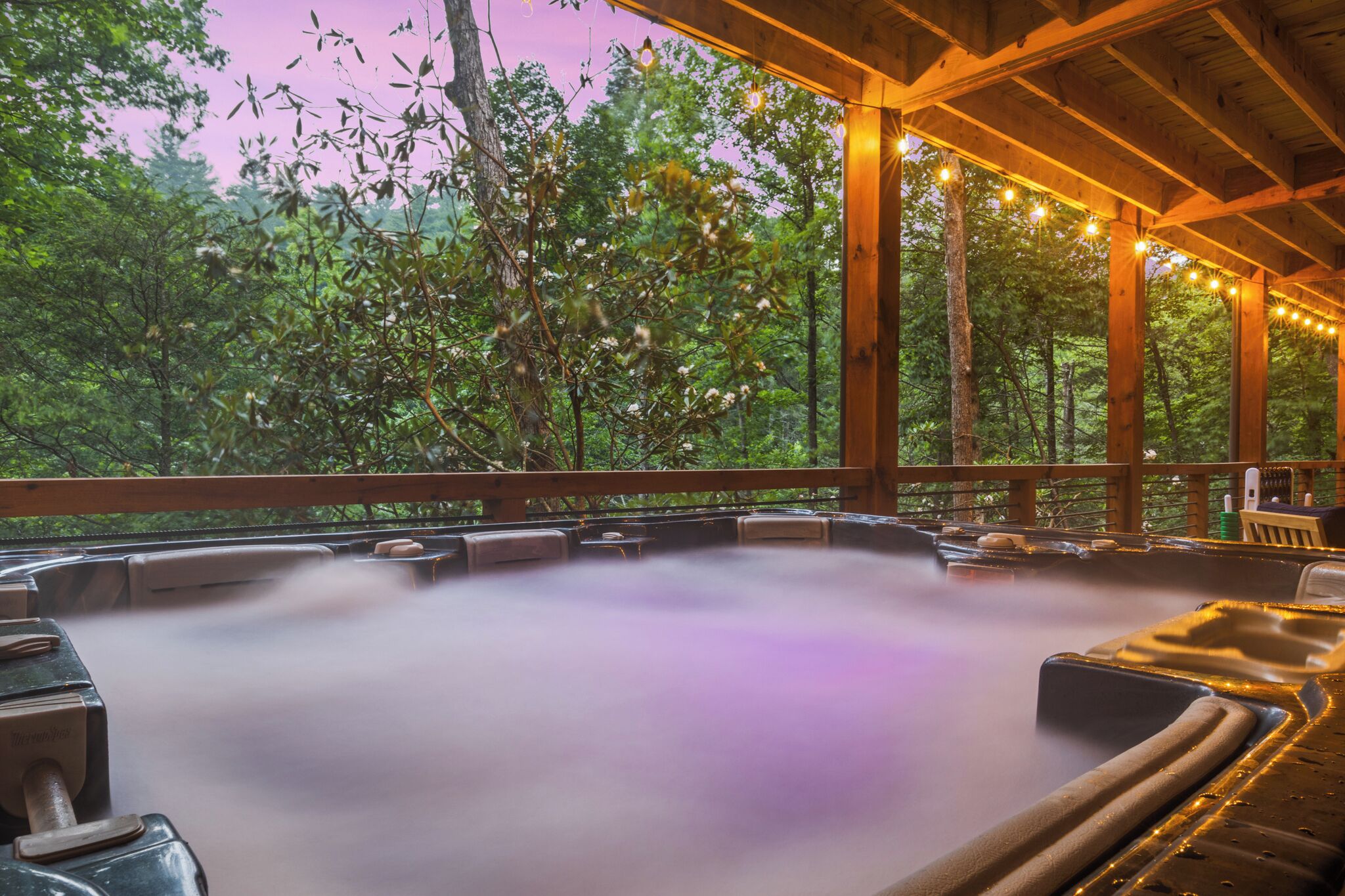 A hot tub area with wooden beams and string lights, surrounded by trees.