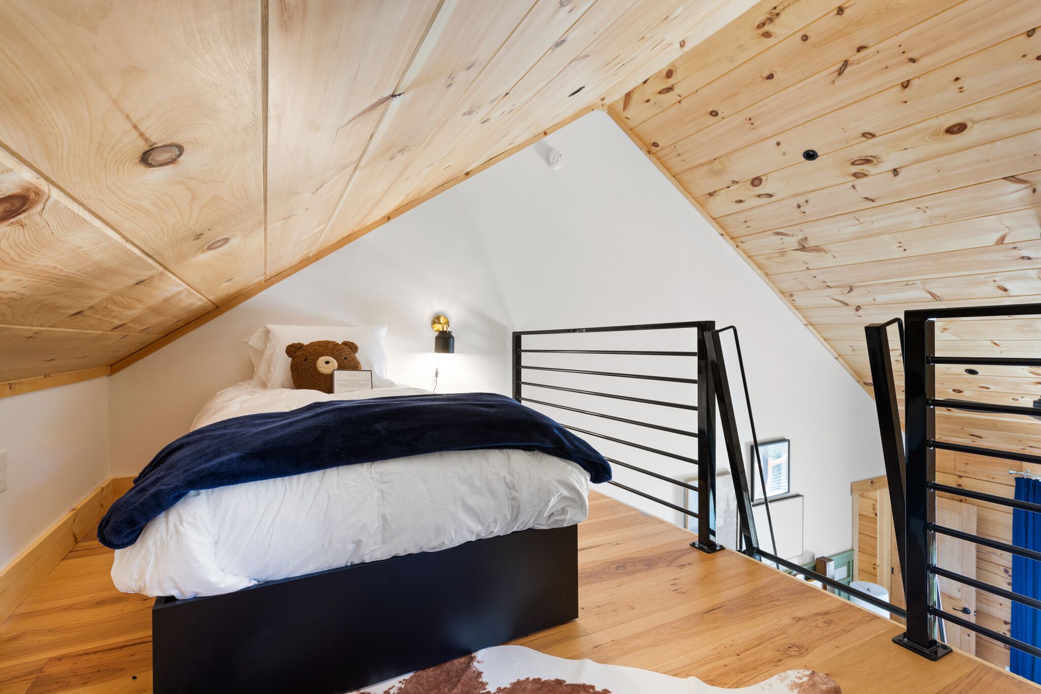 A bedroom with a sloped ceiling, a bed with a black frame, a wooden floor, and a cowhide rug.