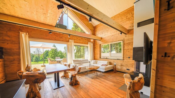 A cozy wooden cabin interior with a dining area, sofa, and fireplace. - "Whisper of Alpacas" chalet (Oederan)