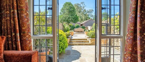 A view through a glass door leading to a stone pathway, a wooden bench, and a garden with various plants.