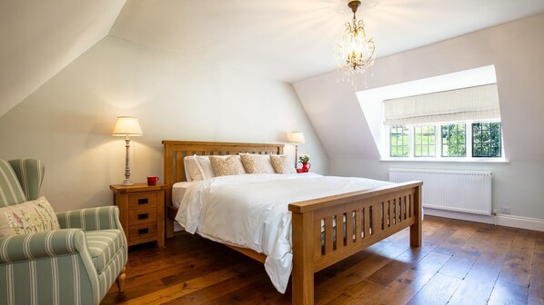 A bedroom with a wooden bed, a nightstand with a lamp, a chair, and a window with a view of greenery. - Hopscotch House - Stanton near Broadway (Near Broadway)
