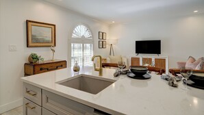 A modern kitchen with a large island, a dining area with a table and chairs, and a living room with a sofa and a flat-screen TV. - LeMalo Vacation Rental: Stylish 1-BR Condo Near 5th Ave S & Gulf Beaches Coastal Vibes, King Bed, and Private Outdoor Space. Perfect Location for Dining, Shopping and Exploring Naples! (Naples)