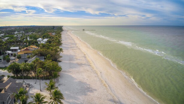 A beach with a pier extending into the ocean, surrounded by residential buildings and palm trees. - LeMalo Vacation Rental: Stylish 1-BR Condo Near 5th Ave S & Gulf Beaches Coastal Vibes, King Bed, and Private Outdoor Space. Perfect Location for Dining, Shopping and Exploring Naples! (Naples)