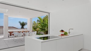 Cozinha moderna com uma ilha grande, armários brancos e vista para palmeiras e um terraço.