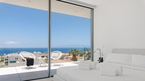 Quarto moderno com uma cama grande, varanda com vista para o mar e uma cadeira branca.