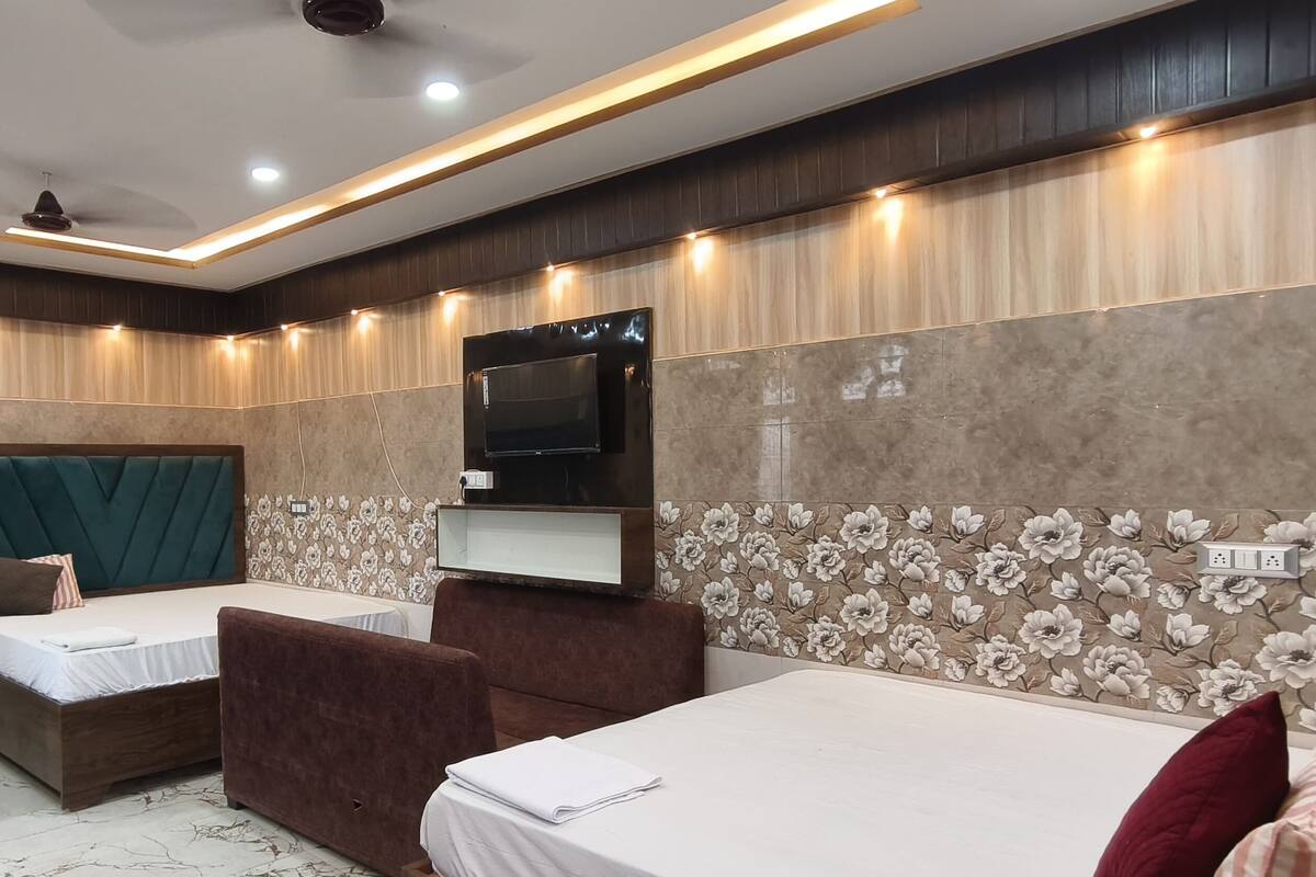 A hotel room with two single beds, a sofa bed, a TV mounted on the wall, and a ceiling fan.