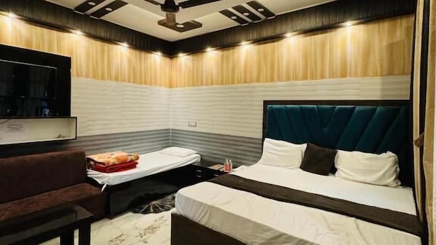 A modern bedroom with two beds, a sofa, a TV, and a ceiling fan. - Hotel Samiksha Inn (Ayodhya)