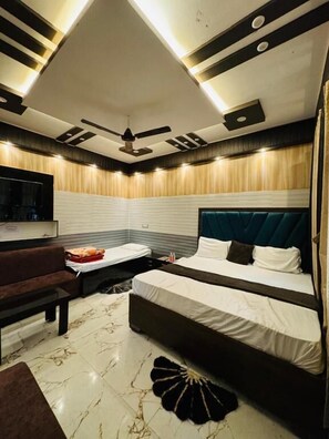 A modern bedroom with two beds, a sofa, a TV, and a ceiling fan. - Hotel Samiksha Inn (Ayodhya)