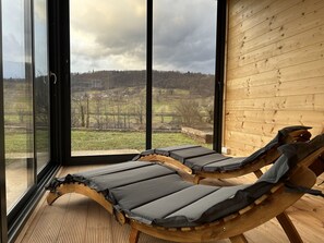 Una habitación con dos sillones de madera orientados hacia un ventanal con vistas a un paisaje rural.