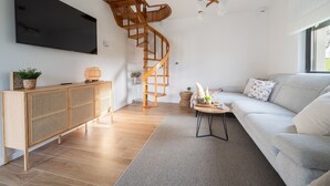 Una sala de estar moderna con una escalera de madera, un televisor de pantalla plana grande, un sofá y un mueble de madera.