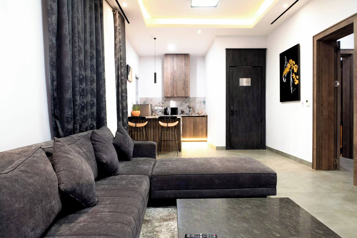 A modern living room with a sectional sofa, a coffee table, and a kitchen in the background.