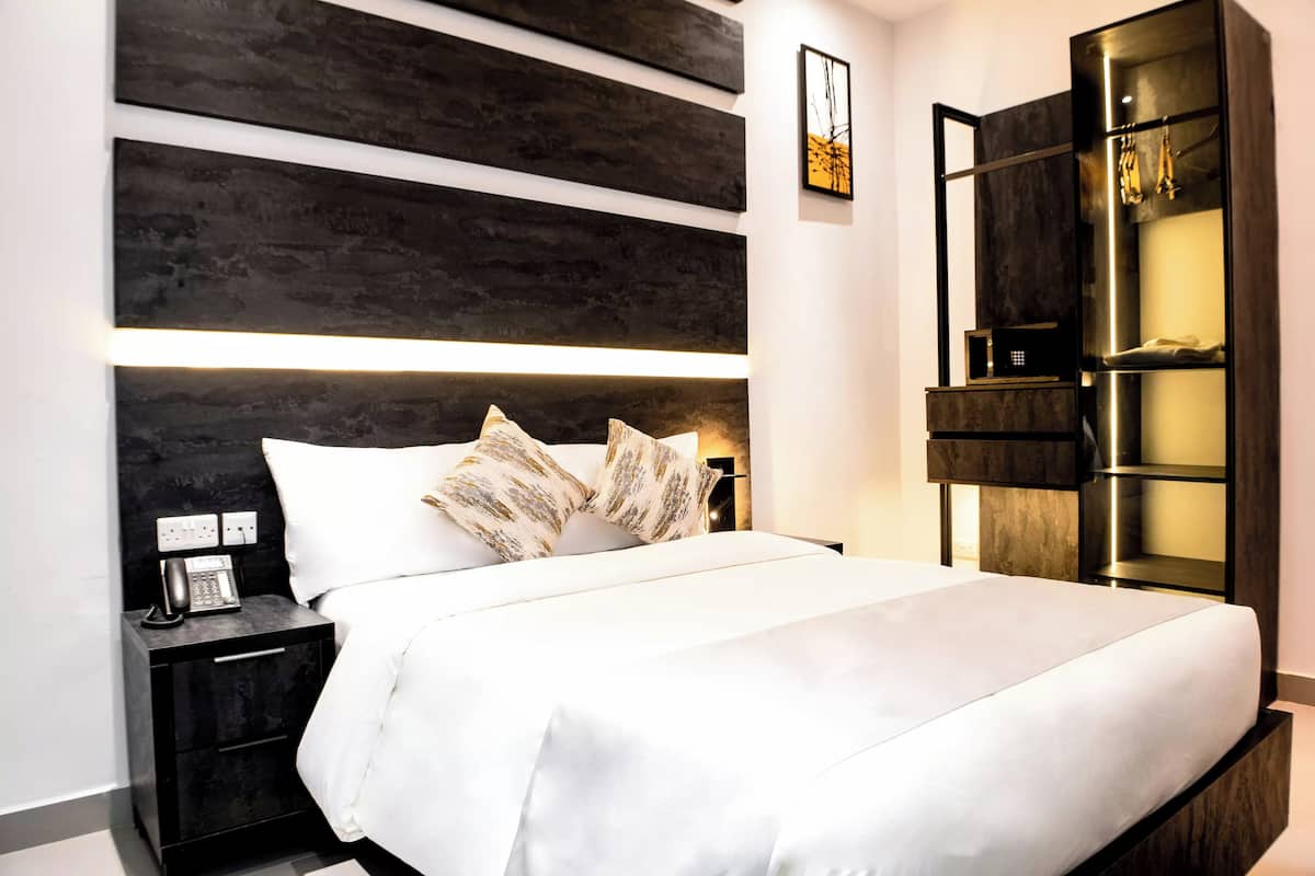 A modern hotel room with a large bed, a bedside table with a phone, and a wardrobe with a mirror.