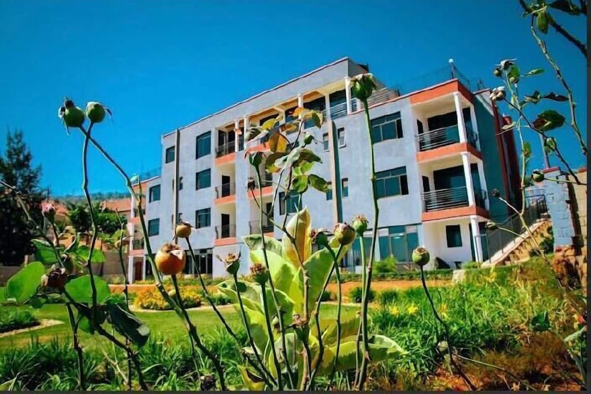A multi-story building with a flat roof, surrounded by greenery and a clear blue sky.
