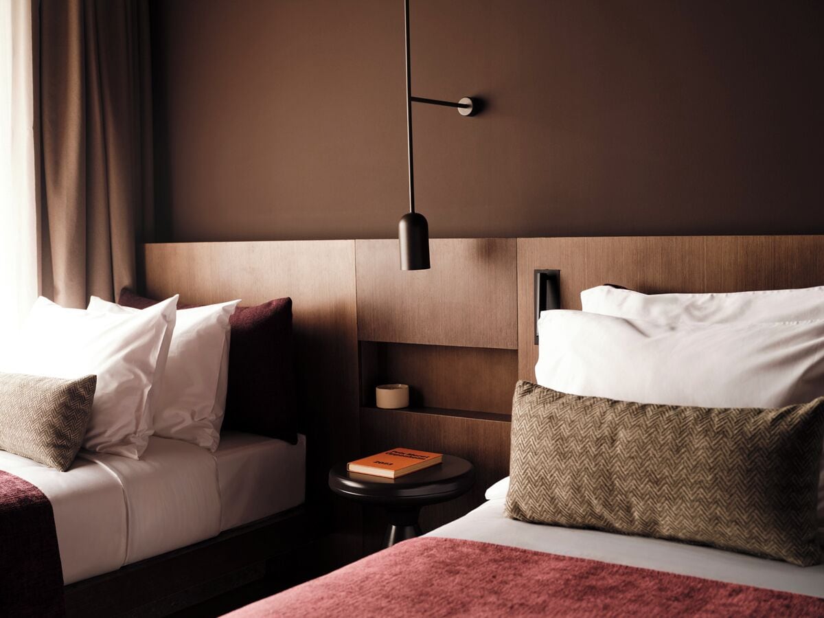 A hotel room with a bed, a bedside table, a lamp, and a nightstand.