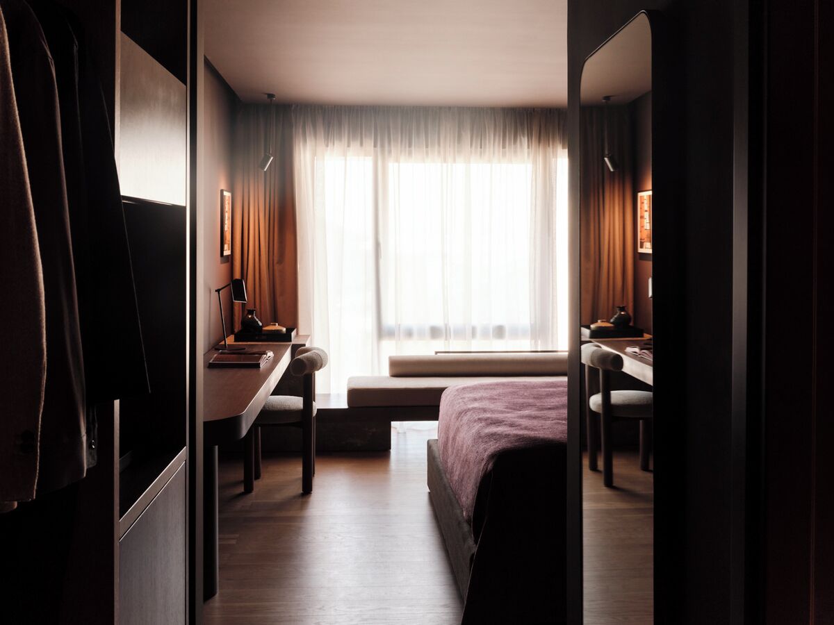 Hotellihuone, jossa on sänky, työpöytä, tuoli ja ikkuna, jossa on verhot.