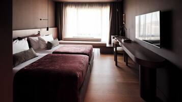 A modern hotel room with two beds, a flat-screen TV, a desk, and a large window with curtains.