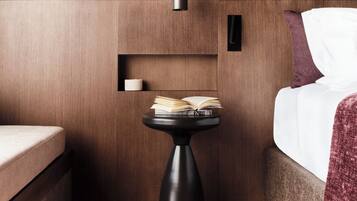 A compact hotel room with a bed, a small black table with an open book, a white pillow, and a wooden wall.