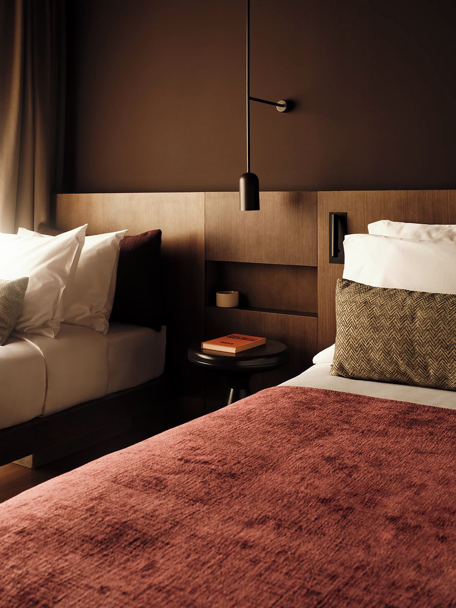 Una habitación de hotel con una cama, un sofá, una mesita de noche con un libro y una lámpara de pared.