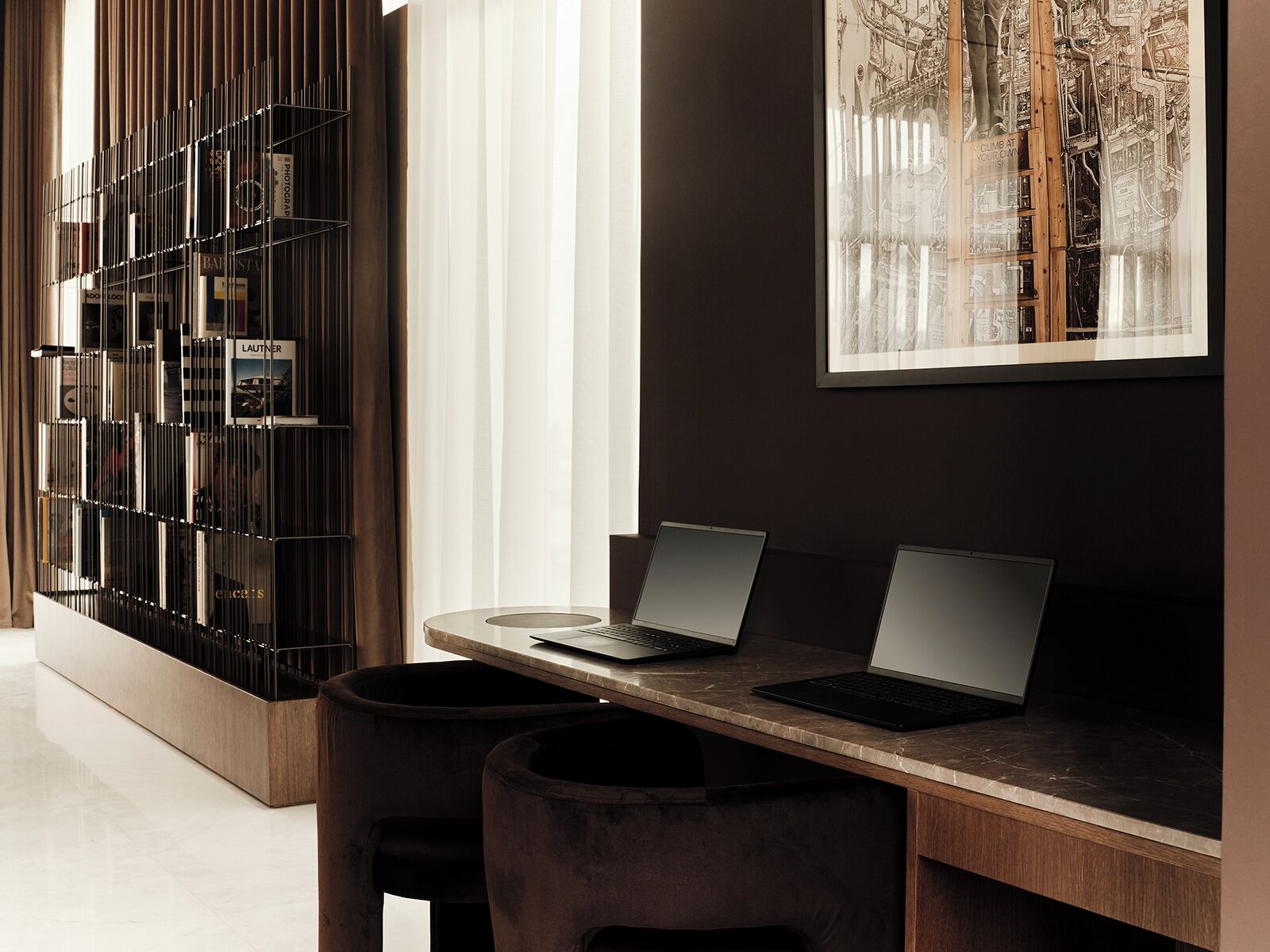 A modern interior with a desk, two laptops, a framed artwork, and a metal bookshelf.