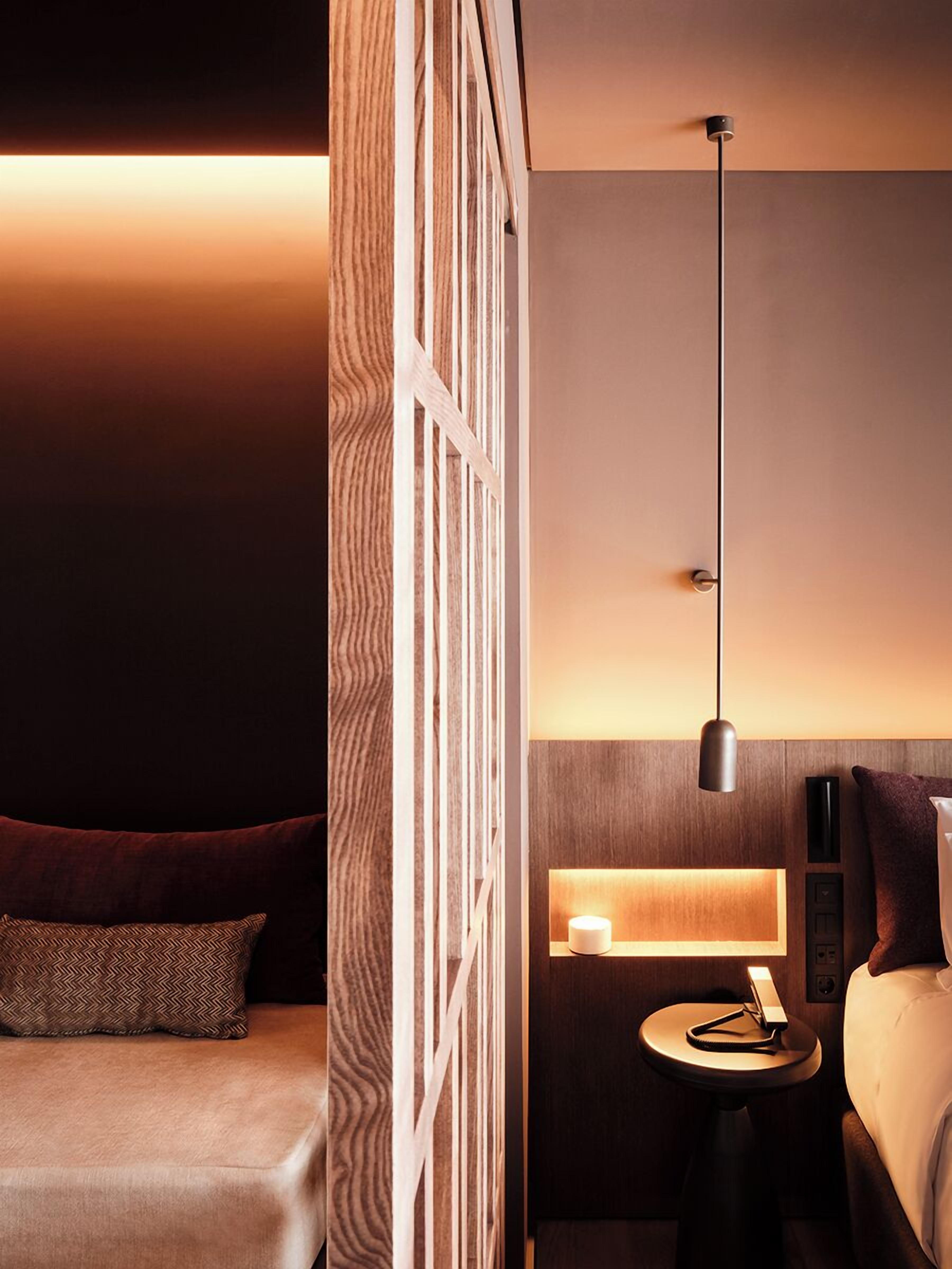 Ein modernes Hotelzimmer mit einem Bett, einem Nachttisch mit Lampe und einer dekorativen Wandverkleidung.