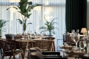 Un restaurante con sillas de mimbre, mesas redondas y plantas en macetas.
