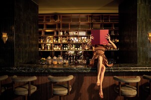 Zona de bar con encimera de mármol, varias estanterías llenas de botellas y taburetes.