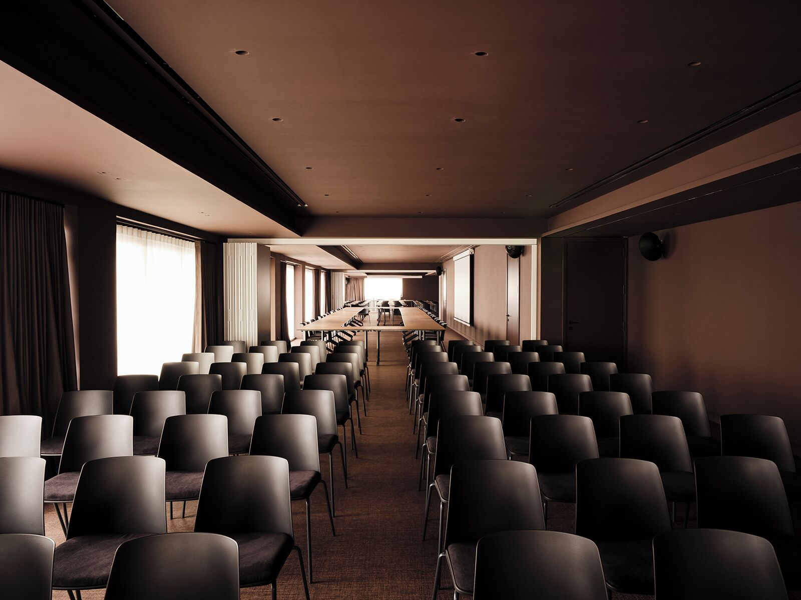 A conference room with rows of chairs, a long table, and large windows.
