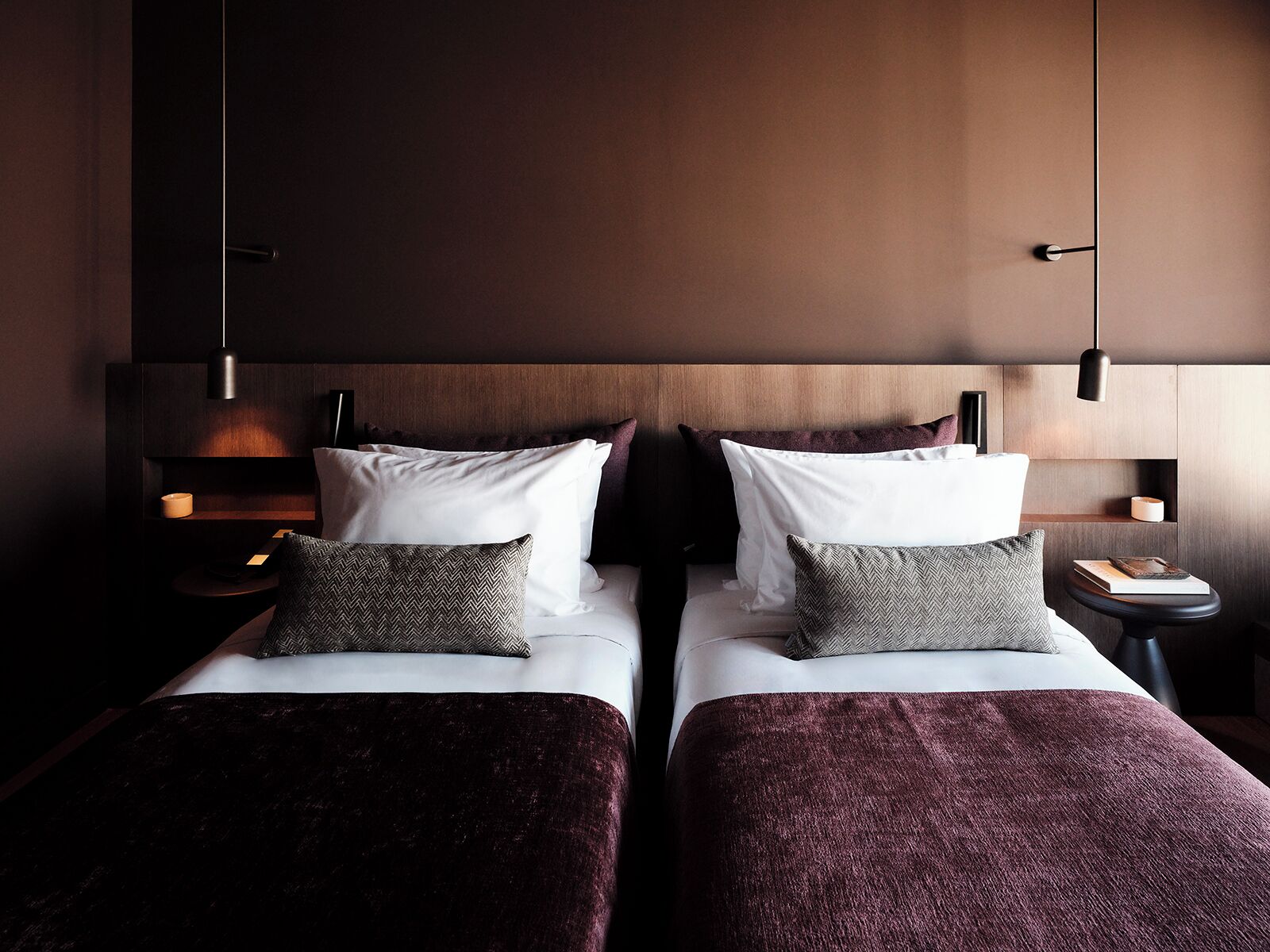 A hotel room with two beds, dark wood headboard, bedside tables with lamps, and a large mirror.