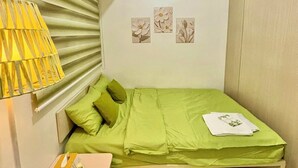 Un dormitorio pequeño y ordenado con una cama individual, una mesita de noche con una lámpara y un par de zapatillas sobre una alfombra verde.