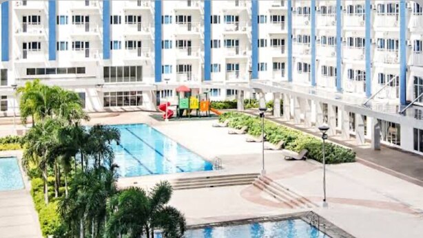 Un hotel moderno con varios balcones, una piscina central y abundante vegetación.