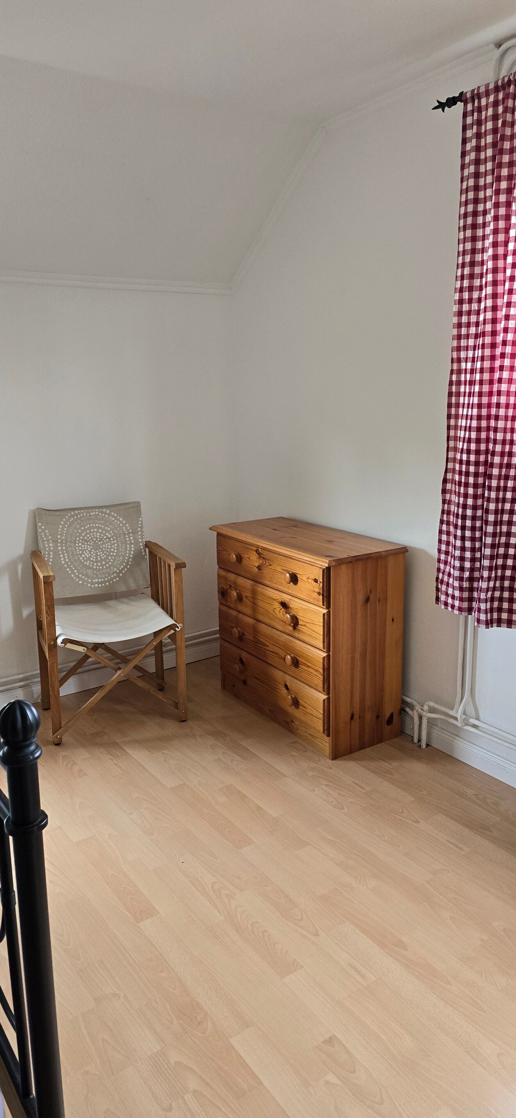 A room with a wooden chair, a wooden dresser, and a red and white checkered curtain.