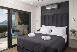 Un dormitorio moderno con una cama grande, un ventanal corredero a un balcón y un aire acondicionado instalado.