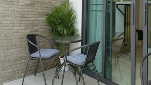 Un área de estar moderna al aire libre con dos sillas, una mesita pequeña, una planta en maceta y un ventanal de vidrio que da a un espacio interior.
