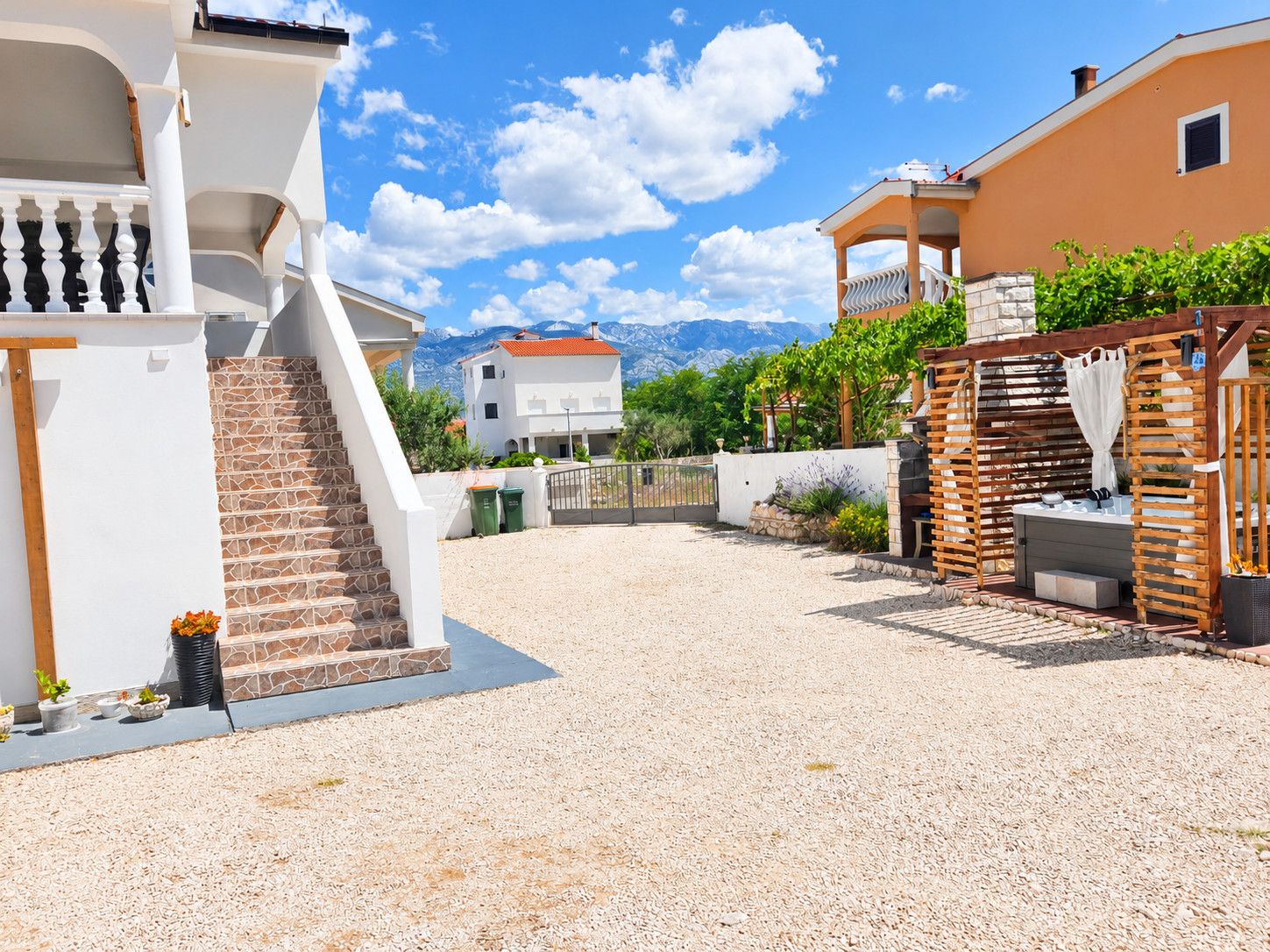 Ein Wohnhaus mit einer Steintreppe, einer überdachten Sitzgelegenheit und Bergblick im Hintergrund.