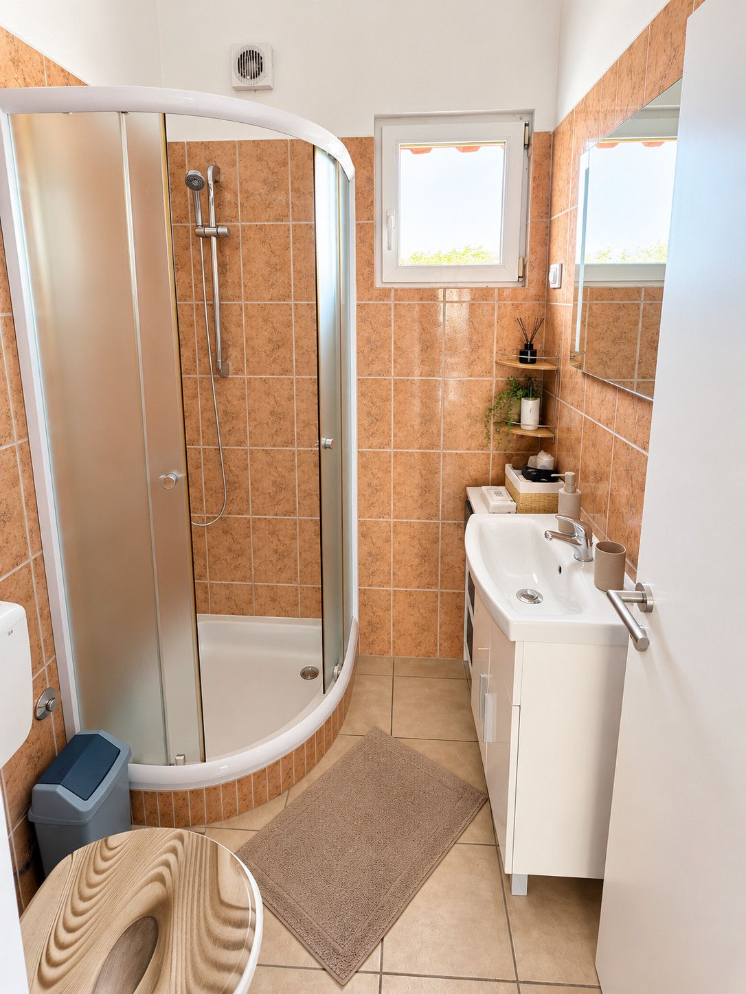 Un baño moderno con ducha de vidrio, lavamanos blanco y una ventana pequeña.