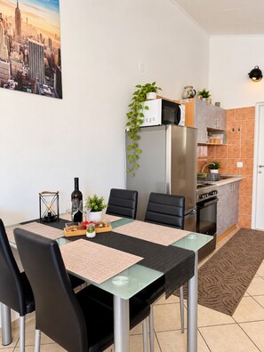 Eine kompakte Küche mit Kühlschrank, Mikrowelle und Herd, ein Essbereich mit Tisch und Stühlen sowie ein Stadtbild an der Wand.