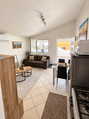 Eine moderne Küche mit Herd, ein Essbereich inklusive Tisch und Stühlen, eine Couch und ein großes Fenster mit Blick nach draußen.