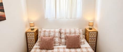 A bedroom with a bed, two bedside tables, a window with curtains, and two lamps.