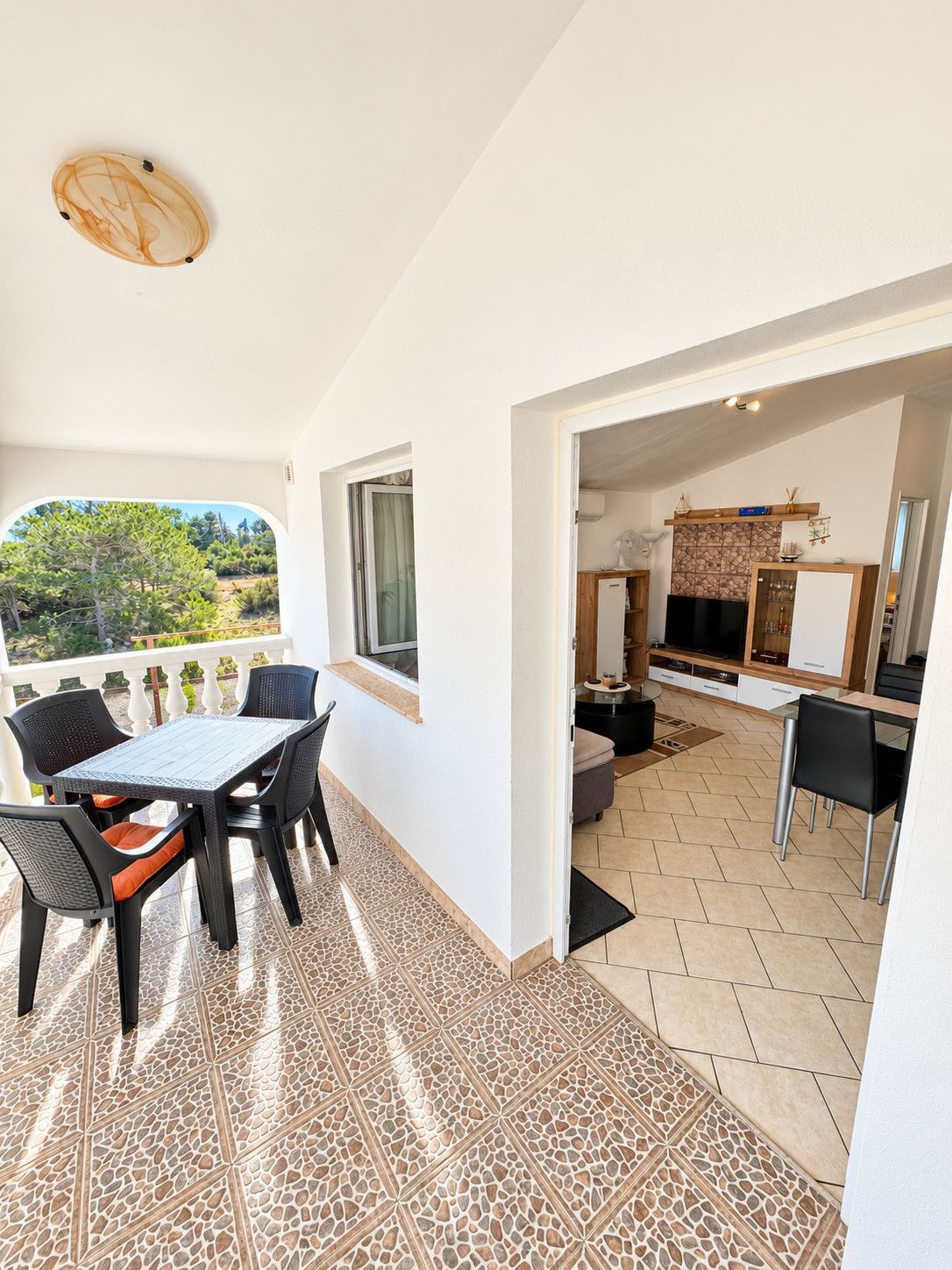 A modern kitchen with a stone backsplash, a dining area with a table and chairs, and a view of a garden through a window.