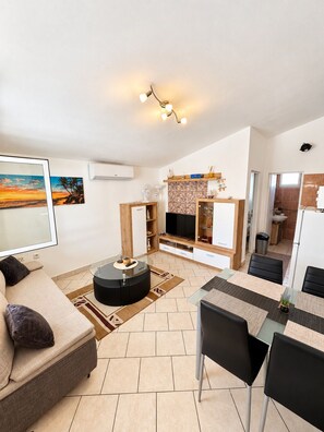 A modern living room with a sofa, a glass coffee table, and a dining area with chairs and a table.