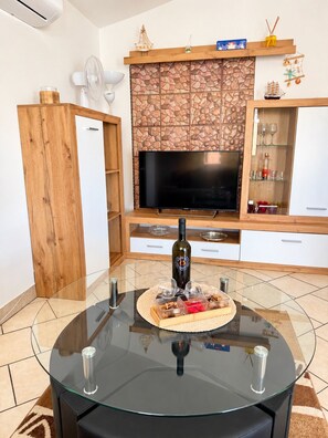 A modern living room with a glass table, a flat-screen TV, and a stone-patterned wall. - Apartment Didovi Dvori 2 with jacuzzi (Ražanac)