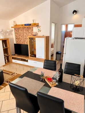 A modern living room with a flat-screen TV, wooden entertainment unit, dining area with chairs and a table, and a kitchen area with a refrigerator. - Apartment Didovi Dvori 2 with jacuzzi (Ražanac)