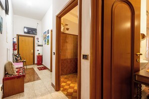 A hallway with a wooden door, a small red cabinet, a chair with a cushion, and a television mounted on the wall. - DI TUTTO E DI PIù (Milan)