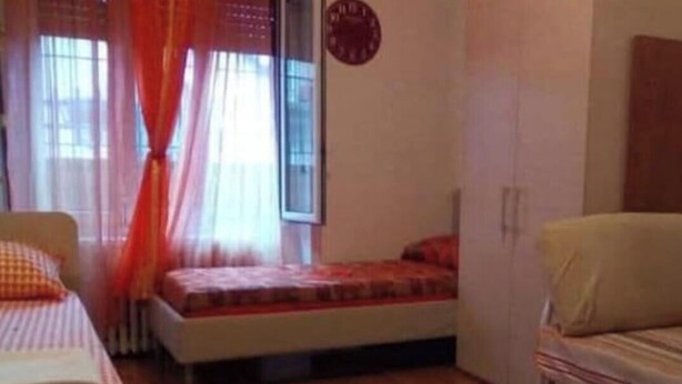 A room with a bed, a small table, a chair, a window with curtains, and a clock on the wall. - DI TUTTO E DI PIù (Milan)